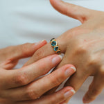 Close-up of a hand wearing a gold ring with blue gemstones on a white background