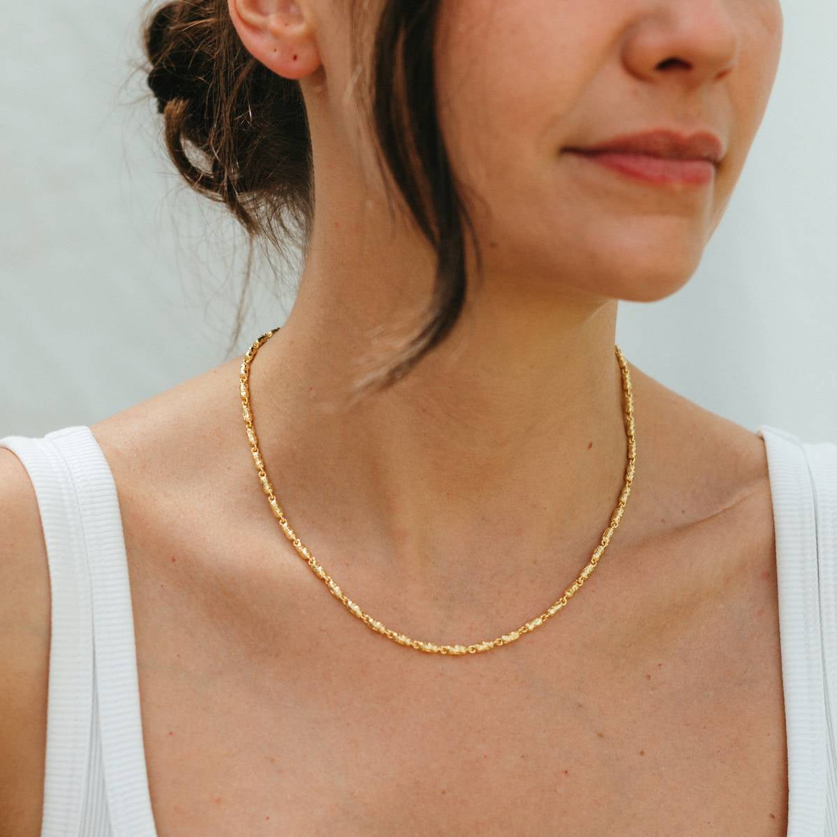 Woman wearing a gold necklace against a plain background