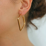 Gold geometric hoop earring worn by a person with a blurred background
