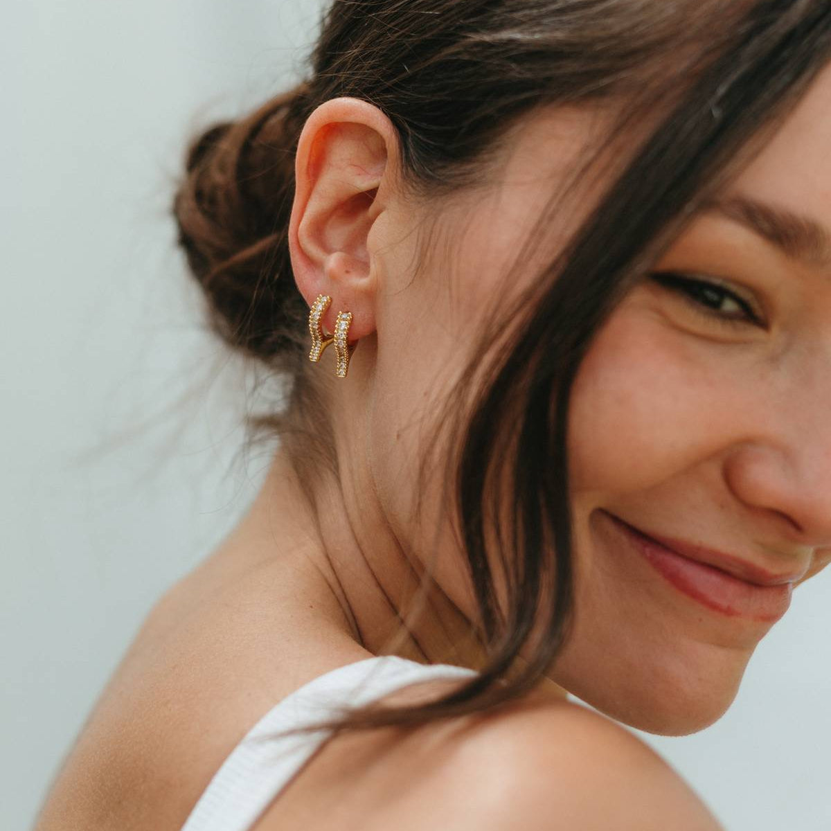 Woman with a side bun wearing gold earrings against a light background