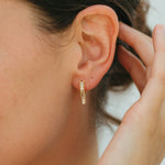Close-up of a person wearing a gold hoop earring with a blurred background