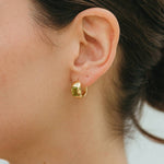 Close-up of a person wearing gold hoop earrings with a blurred background