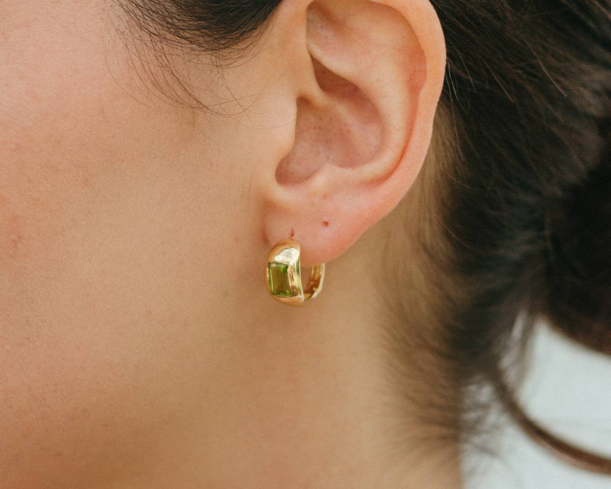 Close-up of a person wearing gold hoop earrings with a blurred background