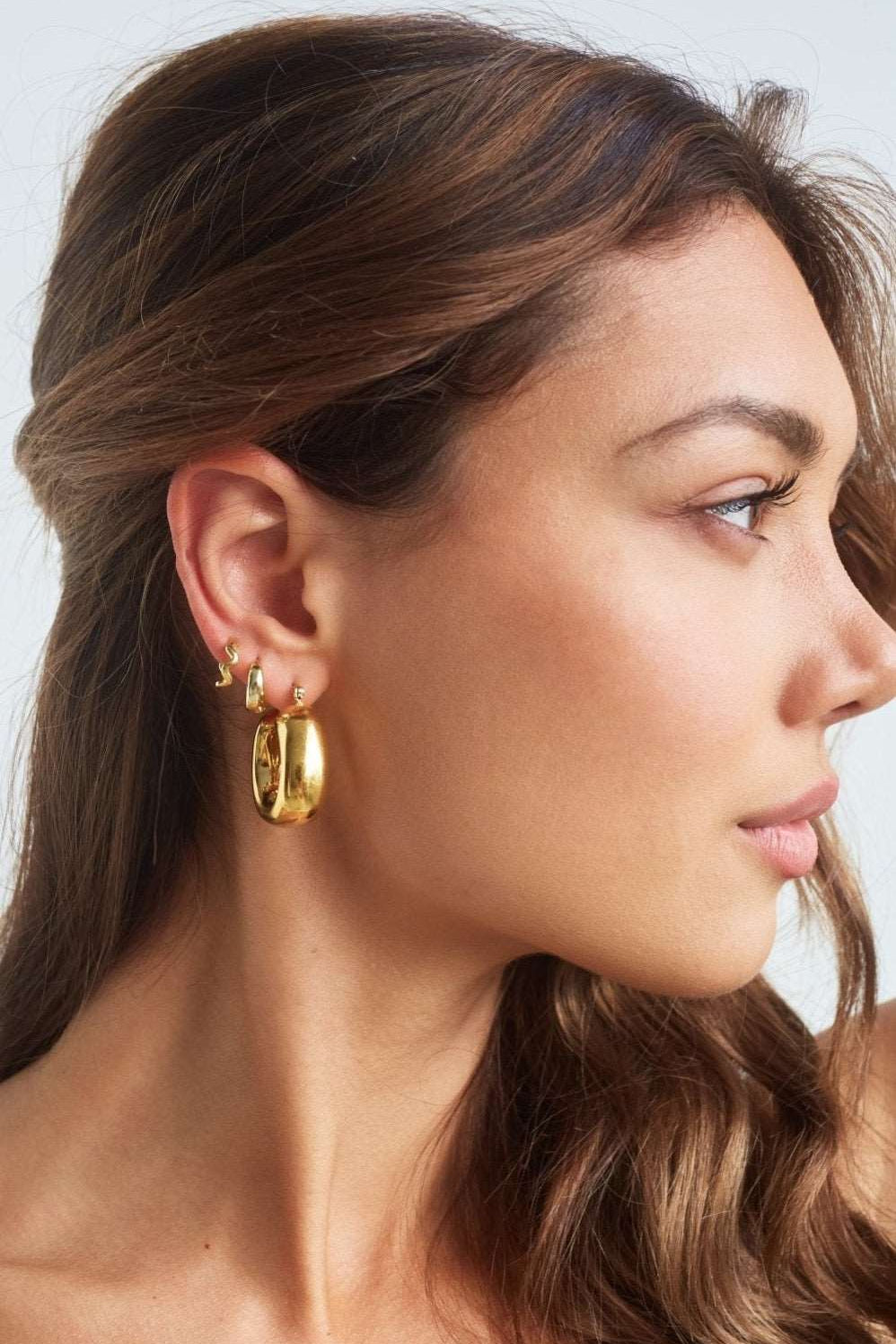 Model wearing large bold square shaped gold hoops 